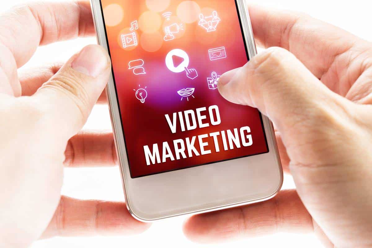 deux mains tenant un telephone portable avec mot et icones de marketing video