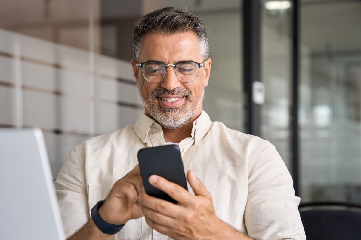 homme d'affaires souriant en lisant le journal interne de l'entreprise sur son téléphone